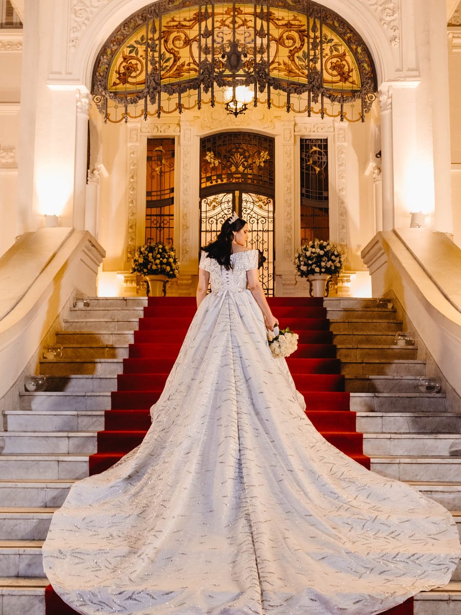 Noiva com cauda longa na escadaria do salão, em casamento produzido pela Rito Eventos