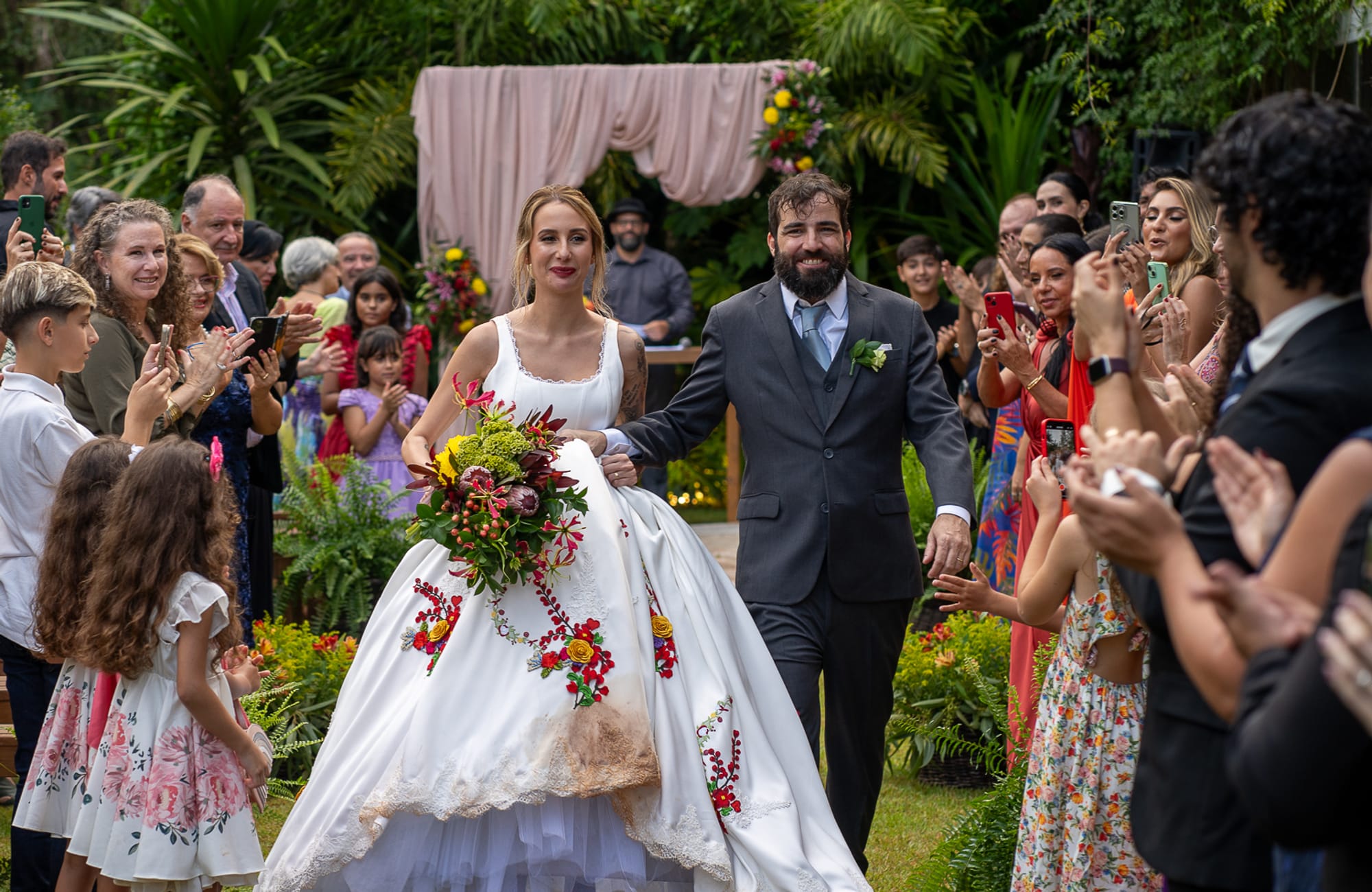 Noivos saindo da cerimônia entre convidados aplaudindo, em casamento ao ar livre produzido pela Rito Eventos
